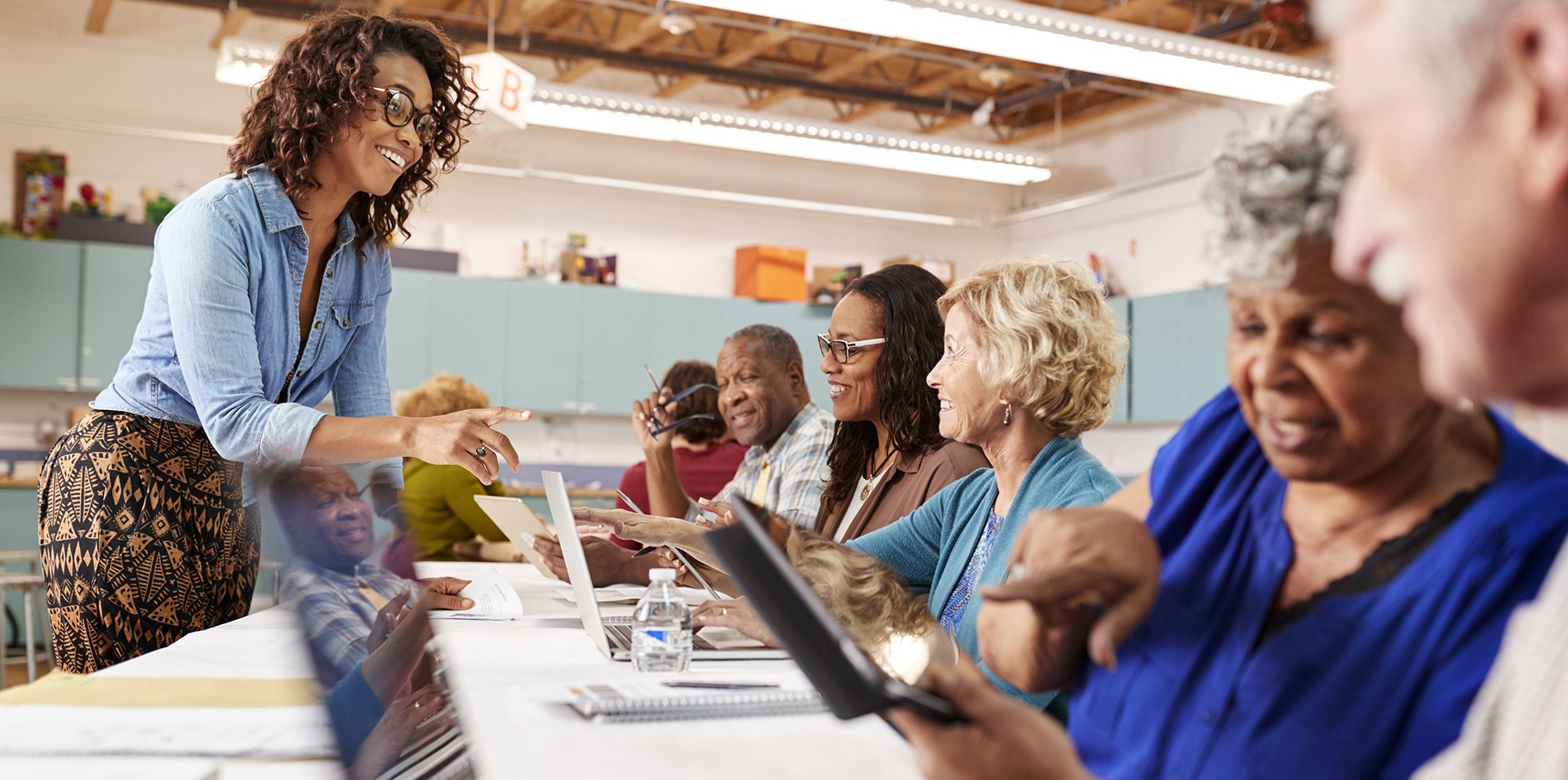 A diverse group of adults smile as they work on laptops and notepads in a creative studio space.