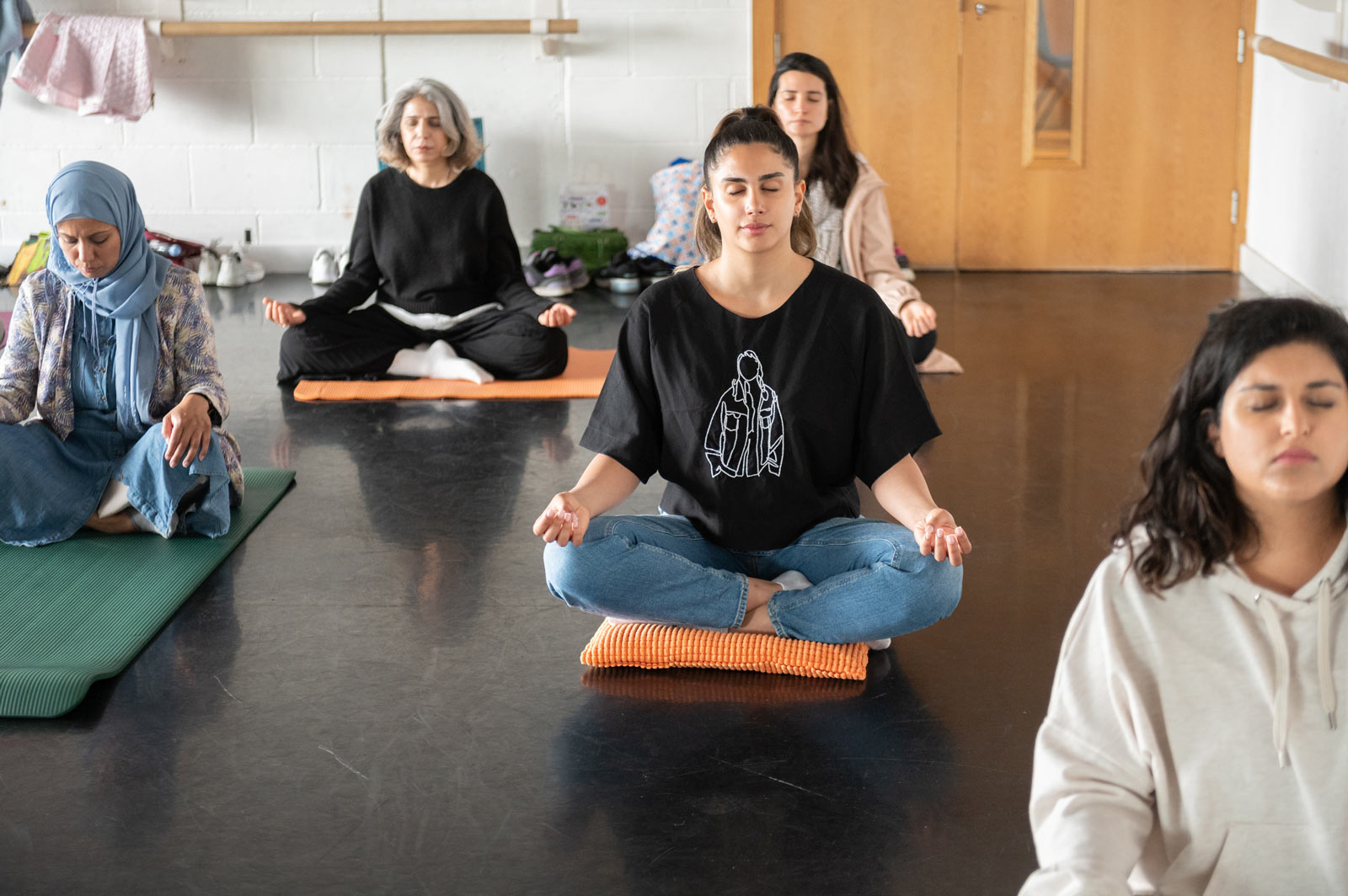 A yoga class taking place in the Dance Space. Five women sit crossed legged on yoga mats.