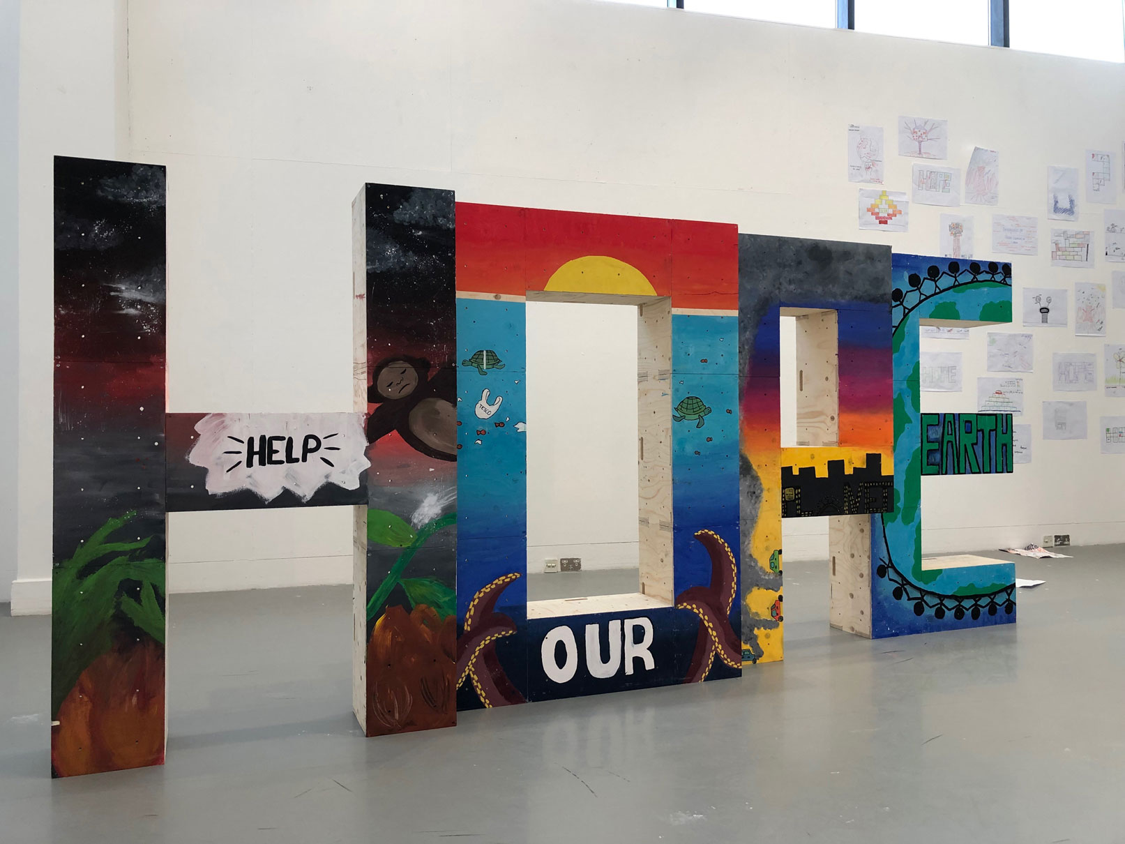 A structure made from painted wooden blocks spelling HOPE on display in a white walled gallery.