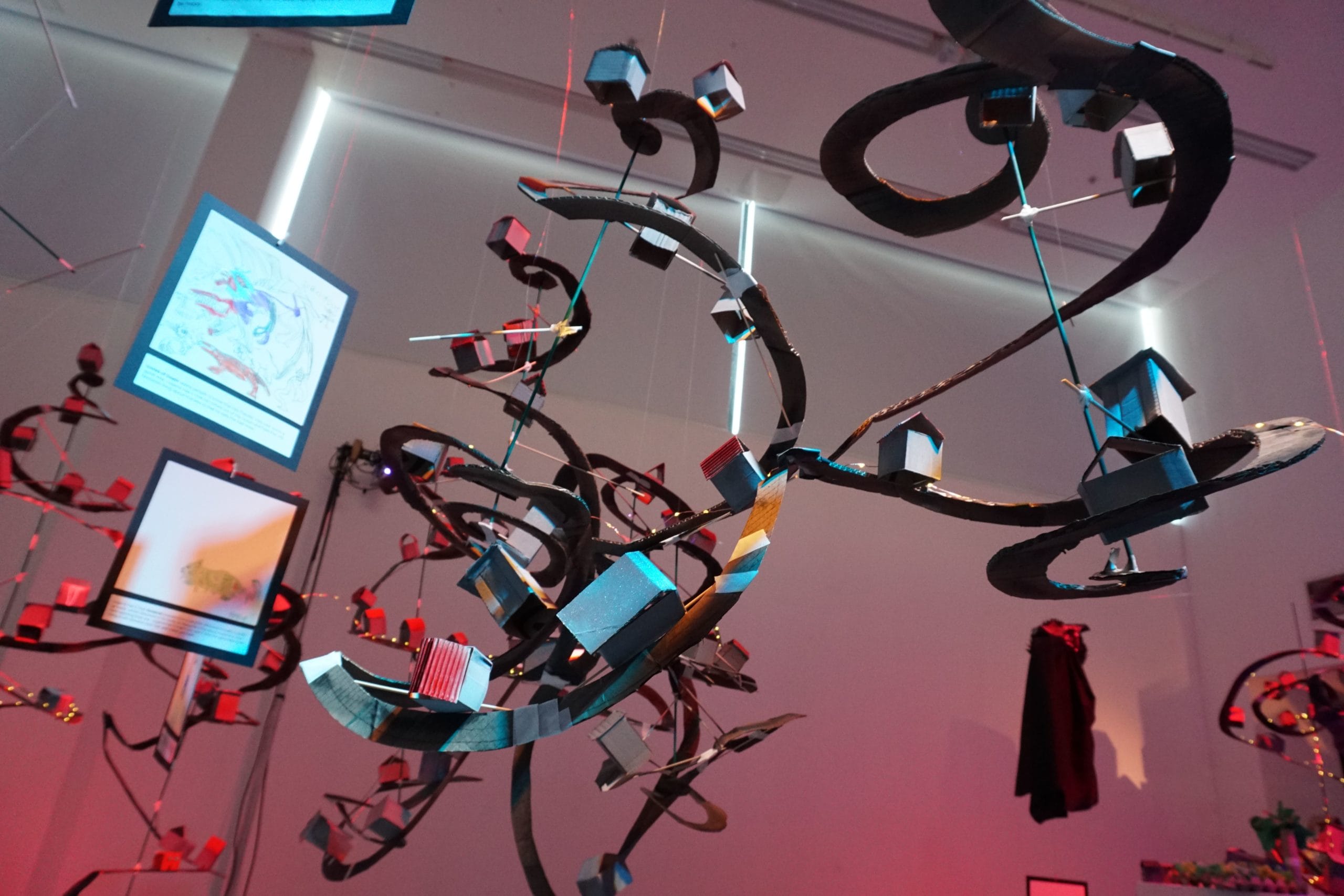 Spiralling cardboard roads are hung from the ceilings, decorated with fairy lights and cardboard houses. This image is photographed from below.